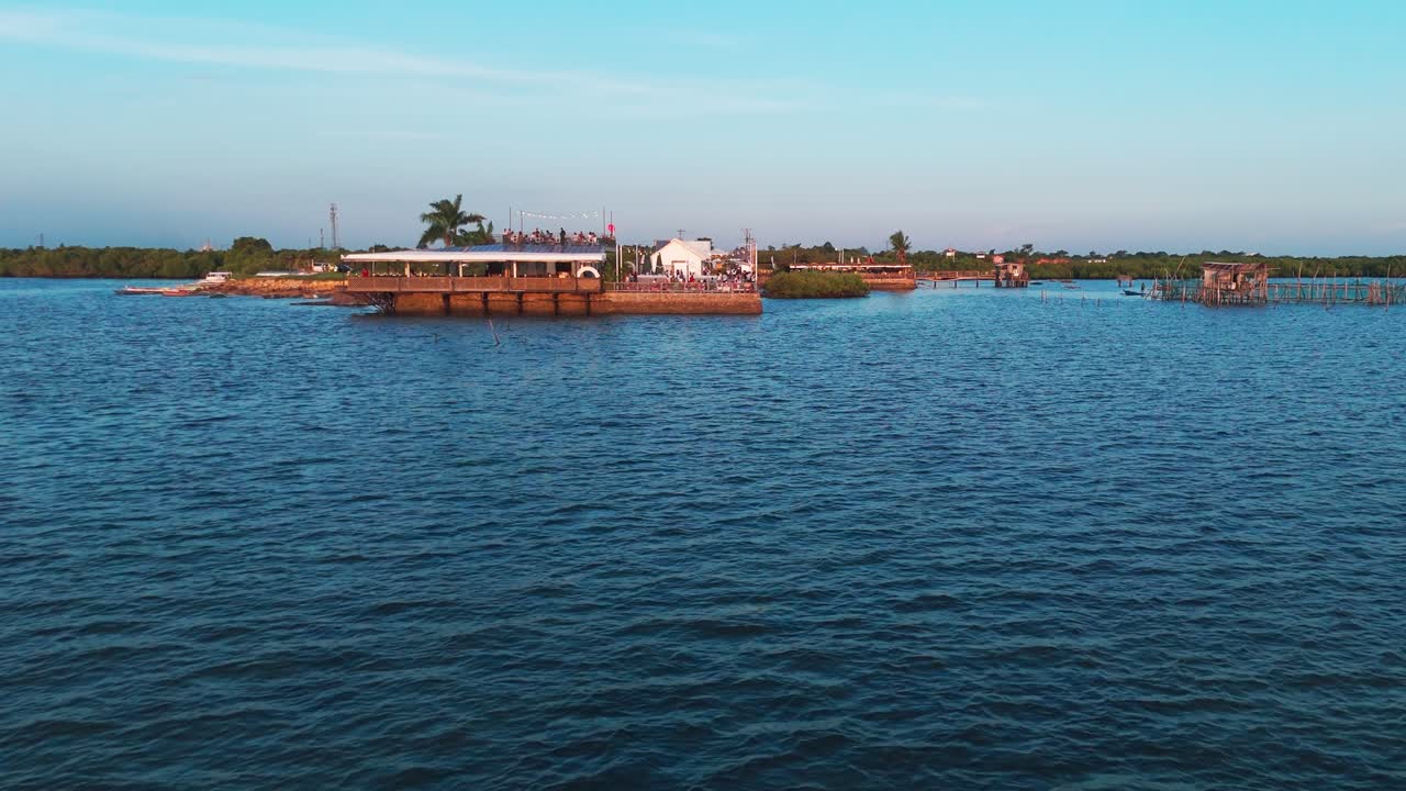 Wide golden hour drone shot of a waterfront restaurant venue alongside traditional fish pens and mangroves in the Philippines. Great for tourism, culture, and coastal lifestyle footage