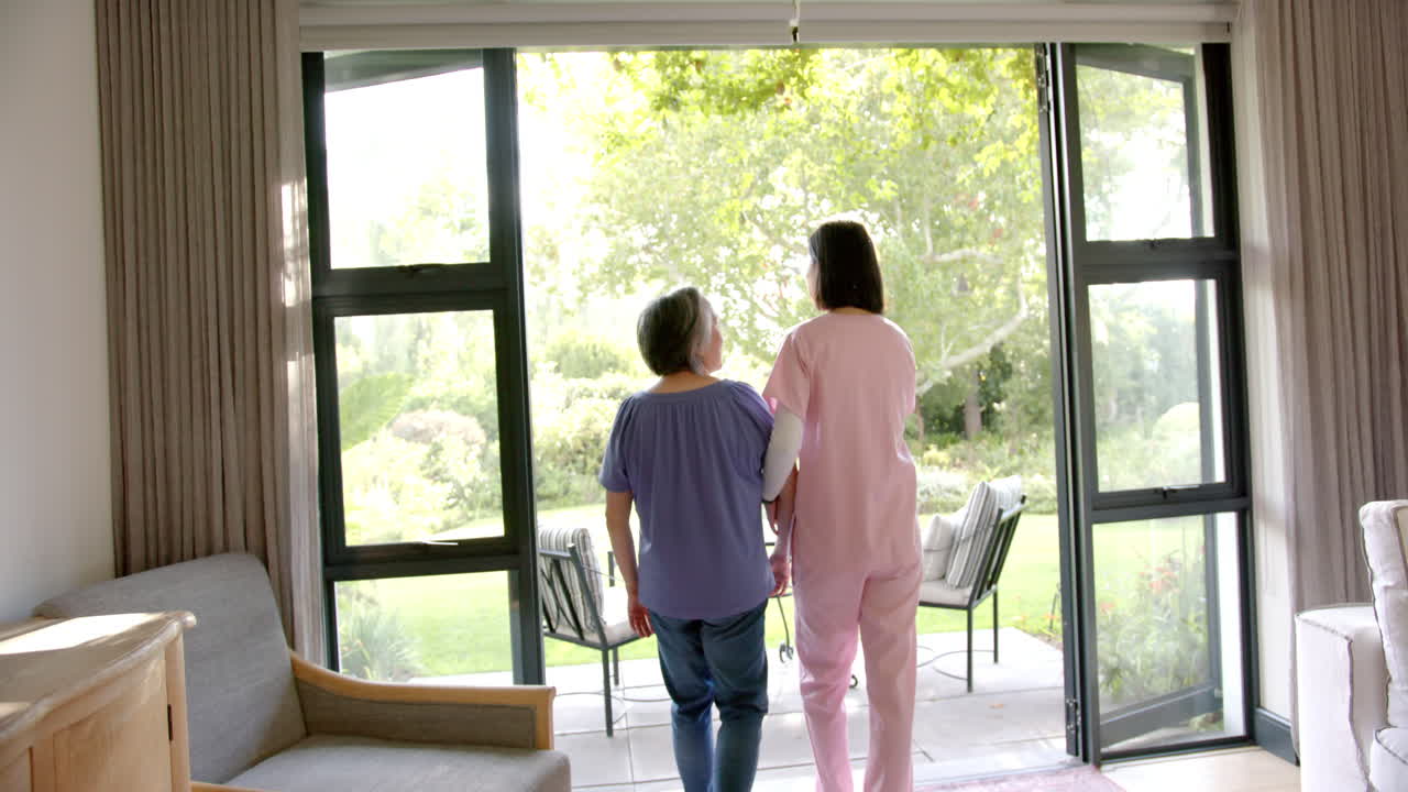 Helping senior asian woman walk, caregiver supporting her in home setting near garden