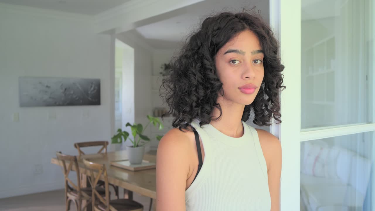 Una donna afroamericana vicino a una porta a vetri, la telecamera ingrandisce, lei si gira, si sistema i capelli, sorridendo verso la telecamera.