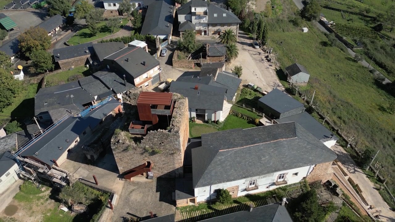 Top-down aerial view of Torre do Castro standing among village houses and rooftops, revealing the medieval stone tower and compact settlement above O Barco de Valdeorras, Galicia