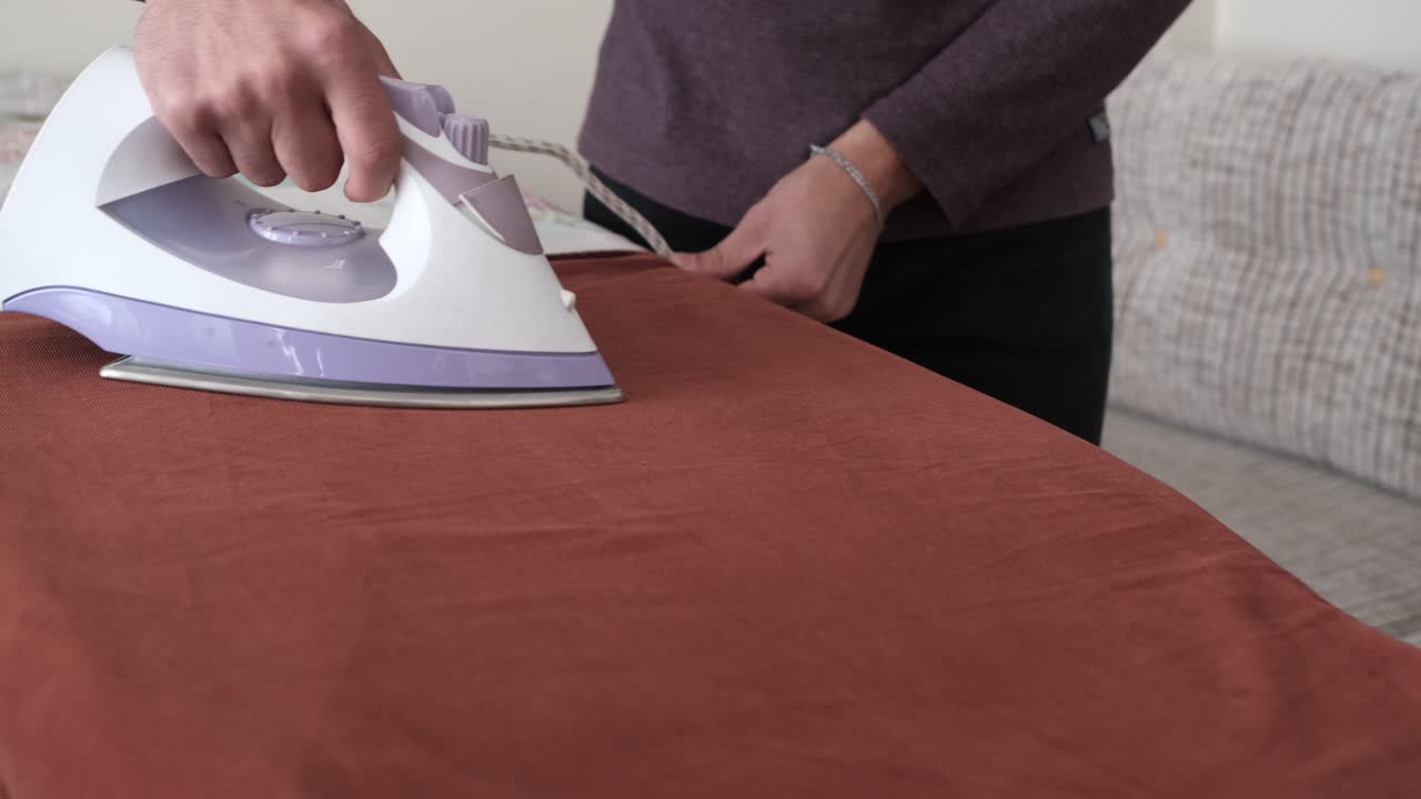 Man ironing the orange shirt on the ironing board at home, people iron before getting dressed, shirt wrinkled
