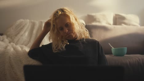 Trauriges-Blondes-Mädchen-In-Einem-Schwarzen-T-Shirt,-Das-Auf-Ihrer-Hand-Zusammengesunken-Ist-Und-Sich-Abends-Zu-Hause-Auf-Dem-Sofa-Einen-Langweiligen-Film-Ansieht