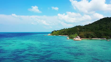 Paradise-tropical-island-with-lush-vegetation-and-palm-trees,-rocky-coastline-washed-by-blue-turquoise-water-of-calm-lagoon,-Thailand