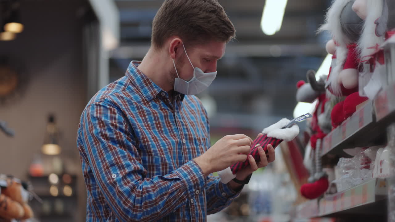 un hombre con una máscara protectora en una joyería y guirnaldas con juguetes para árboles de navidad y en casa. guirnaldas navideñas y decoración