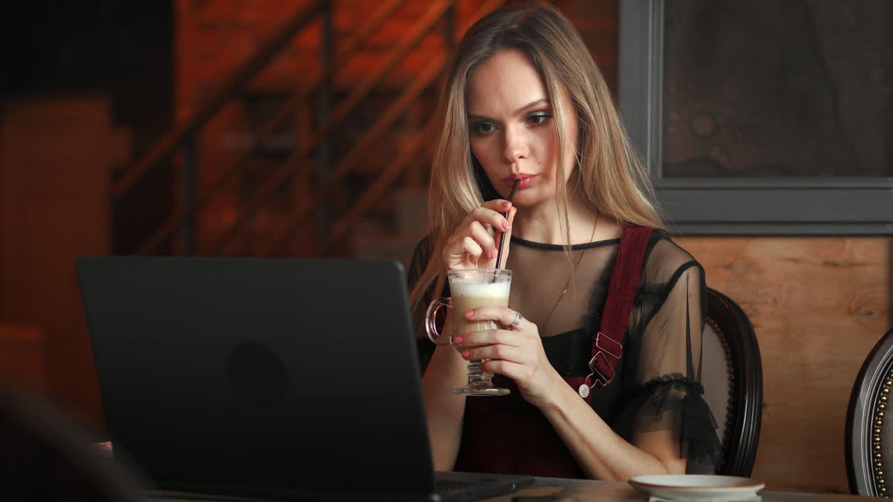 Focused attentive woman in headphones sits at desk with laptop, looks at screen, makes notes, learns foreign language in internet, online study course, self-education on web, consults client by video
