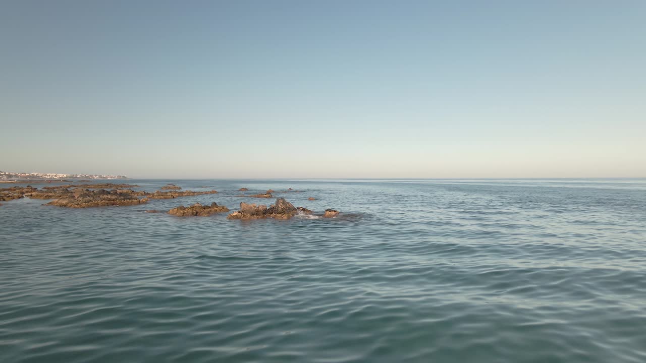 햇볕이 잘 드는 바다를 가로질러 울퉁불퉁한 바위 해안 해변 위로 낮은 각도의 공중 비행