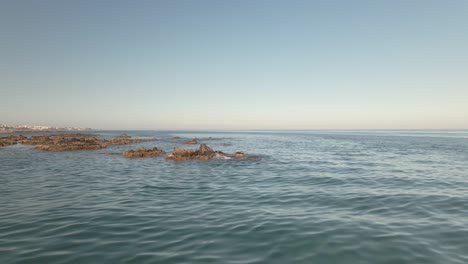 low angle aerial flying over rugged rocky coast beach out across sunny seascape