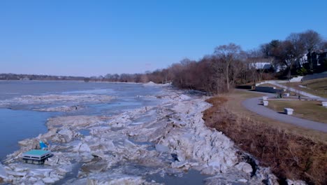 Drone-footage-flying-by-a-park-alongside-a-frozen-river-with-large-fragments-of-broken-ice-and-debris