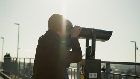 a father lovingly holds his son up to a telescope, guiding him as the boy peers through it with curiosity, the father supports the telescope to ensure a steady view