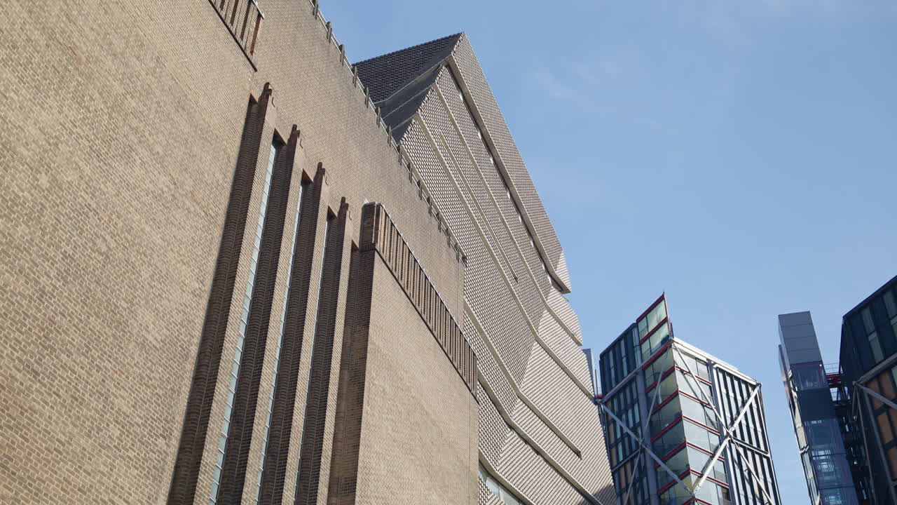Low-angle view of Tate Modern's distinct brick design alongside sleek modern buildings in London's South Bank area, London, England