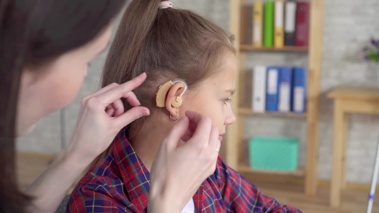 doctor otolaryngologist in the clinic helps to put on the hearing aid to a hearing impaired teenage girl close up