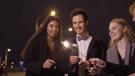 group of friends wearing elegant clothes lighting sparklers in the street after the new year's party