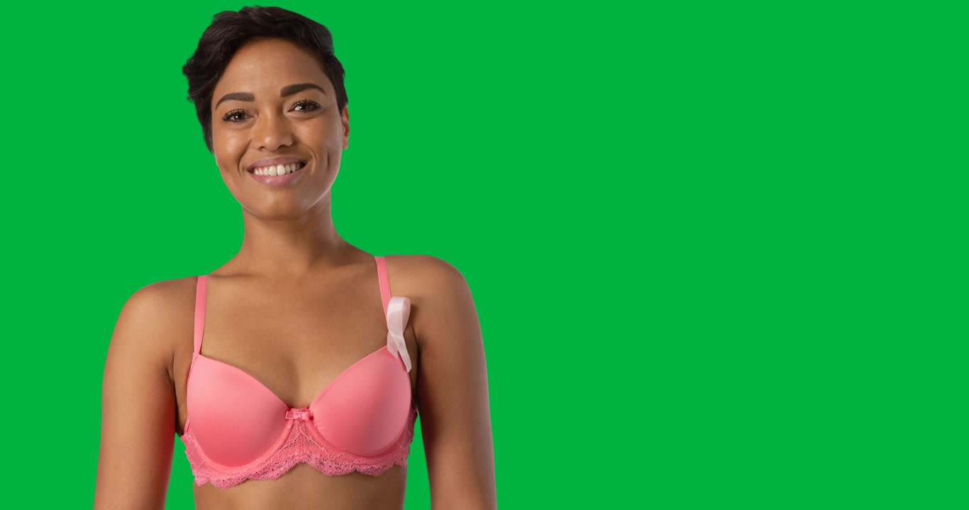 Donna afroamericana che indossa un reggiseno rosa e una spilla a nastro, sorridente su sfondo nero