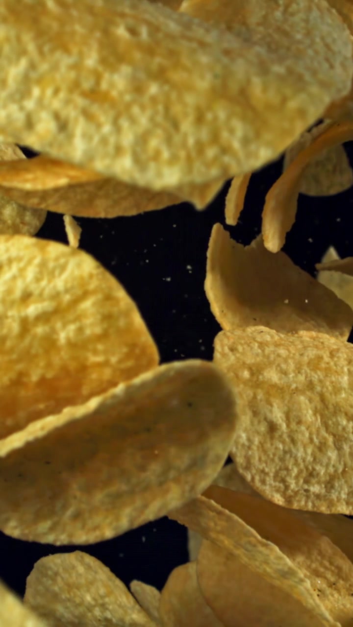 Golden Potato Chips Falling in Slow Motion Against a Black Background