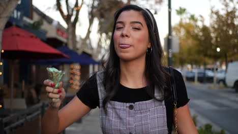 a cute young woman laughing and eating a messy ice cream cone dessert on a city street in slow motion