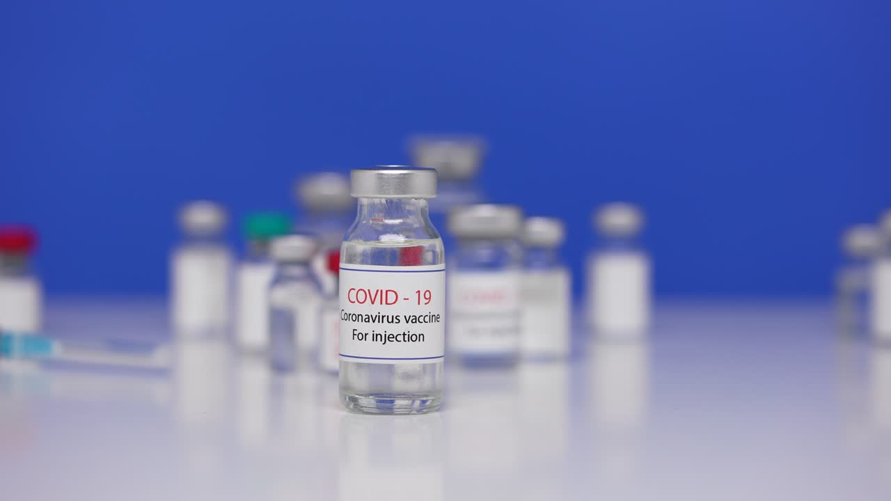botella de vacuna contra el virus sars-cov-2 en la mesa de laboratorio de fondo. ampollas de primer plano con la vacuna del coronavirus covid-19. medicamentos contra la pandemia de ncov. pantalla azul, llave de croma. primer plano. cámara lenta