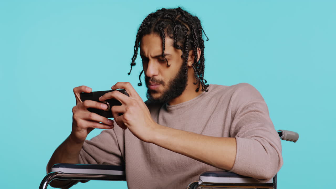 Man with disability plays intense videogame on mobile phone, studio background