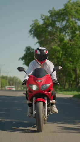 uma motociclista feminina em uma bicicleta elétrica vermelha atravessa uma faixa de pedestres enquanto um carro se move ao lado dela em uma área urbana, o fundo inclui árvores verdes, postes elétricos