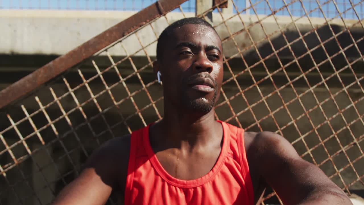 hombre afroamericano cansado bebiendo de una botella de agua, tomando un descanso en el ejercicio al aire libre