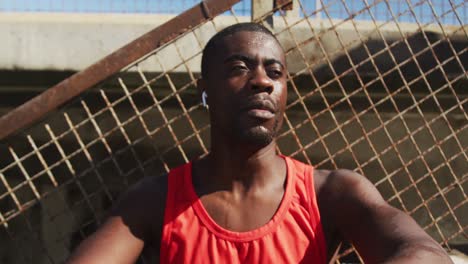 tired african american man drinking from water bottle, taking break in exercise outdoors
