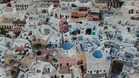 drone view in greece flying over santorini with oia town white houses at close with colored fronts and pools at sunrise