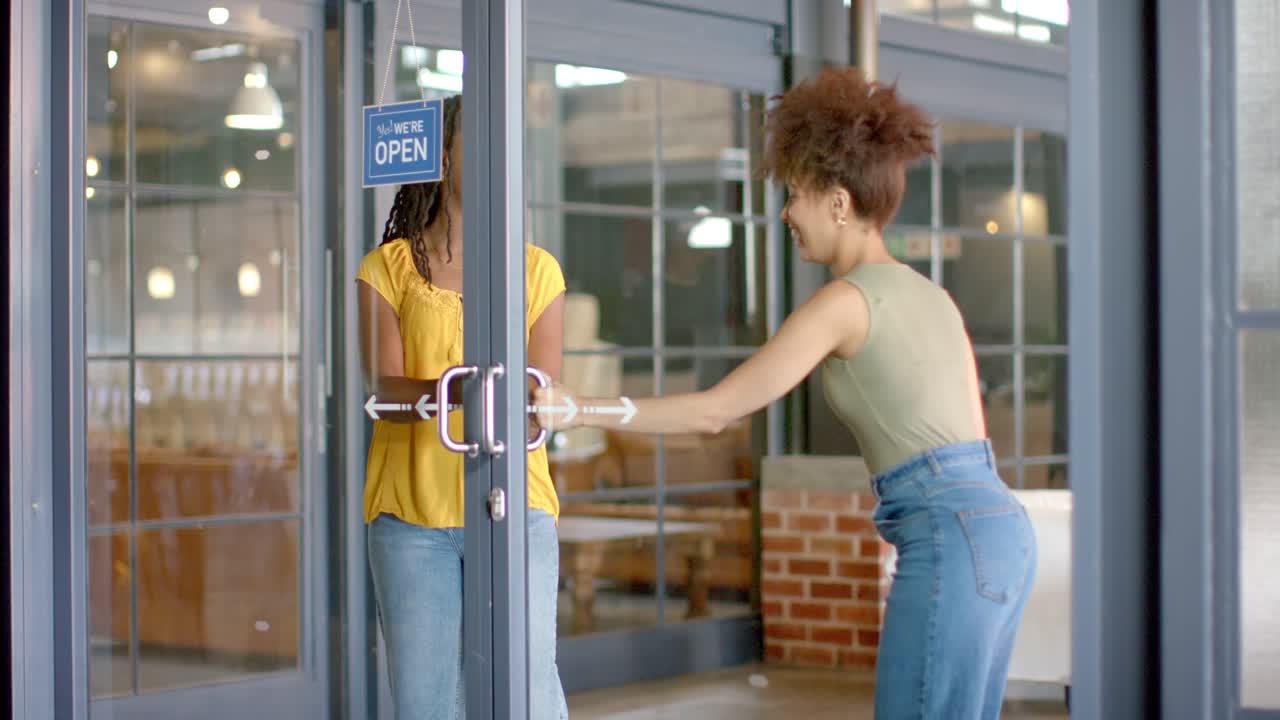 Mujeres afroamericanas con blusa amarilla y camiseta de tirantes verde, volteando el cartel de 'Abierto' y tirando de las manijas para entrar a la cafetería.