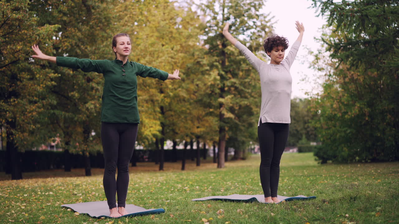Two women practicing yoga in a park during fall