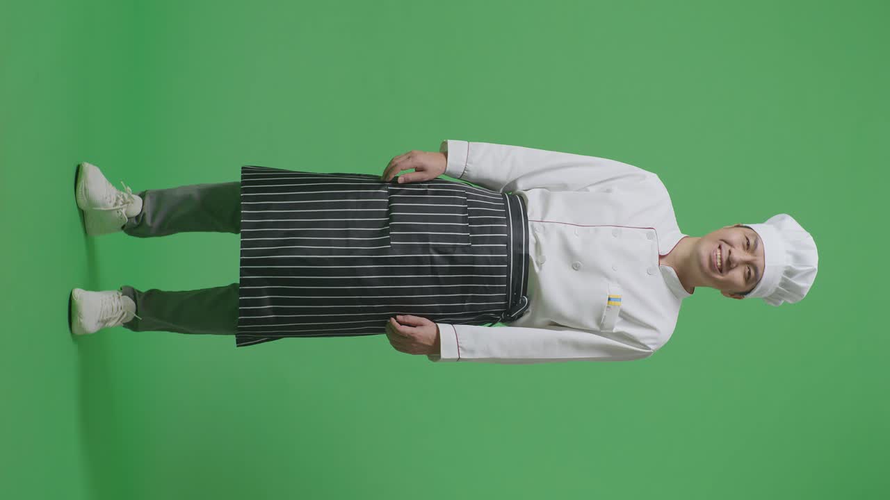 녹색 스크린 배경 스튜디오에서 카메라에 서서 미소 짓는 아시아 남자 셰프의 몸이 가득 차 있습니다.