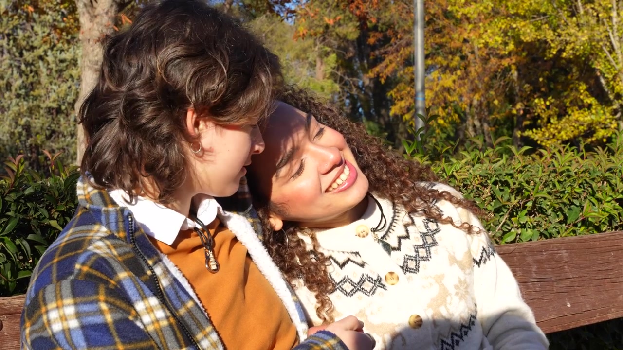 Giovane coppia lesbica affettuosa che parla e sorride insieme su una panchina in un parco autunnale.