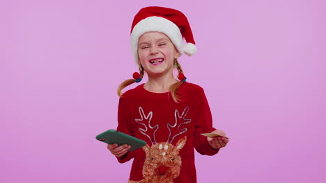girl kid in christmas sweateruse mobile cell phone, plastic credit bank cards, win, calebrate, wow