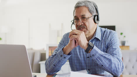 Video-De-Un-Hombre-Birracial-Senior-Feliz-Sentado-En-El-Escritorio-Usando-Auriculares-Y-Una-Computadora-Portátil-Haciendo-Videollamadas