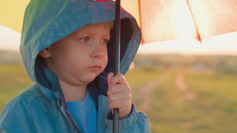 boy stands with parasol in somber mood child stands alone in green field on rainy day with