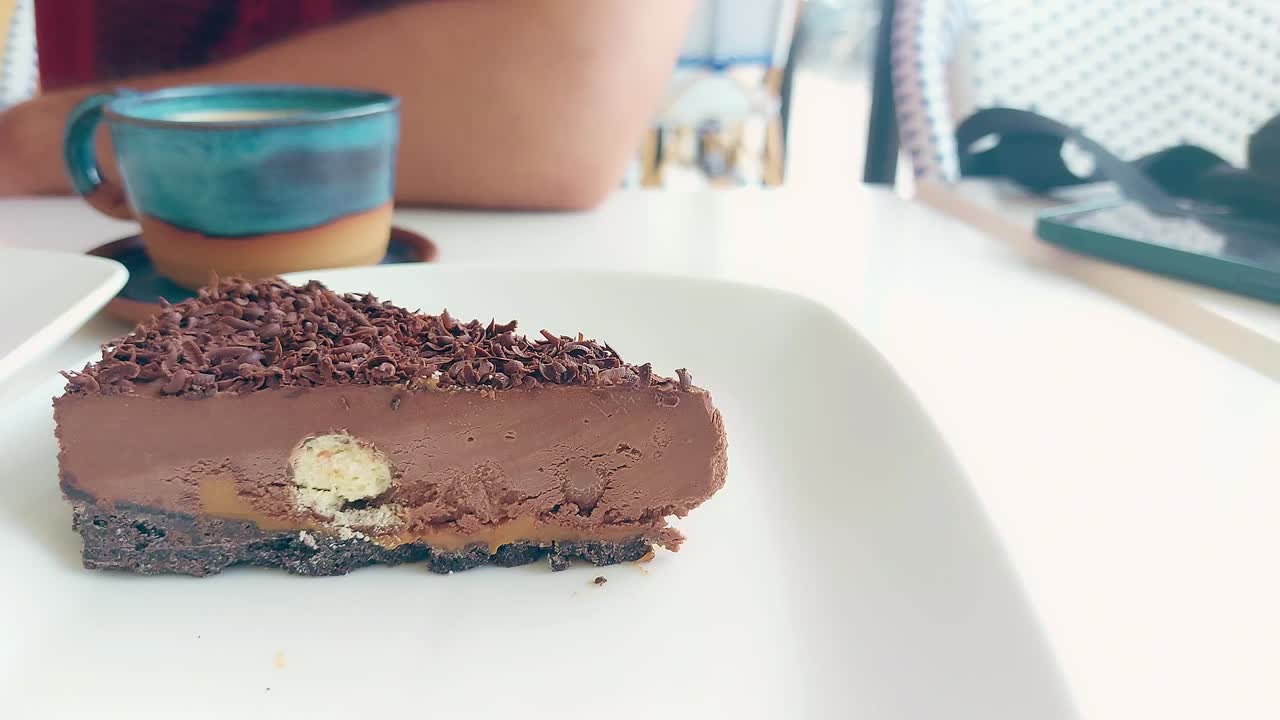 A fork slicing into a rich slice of chocolate cake next to a coffee cup