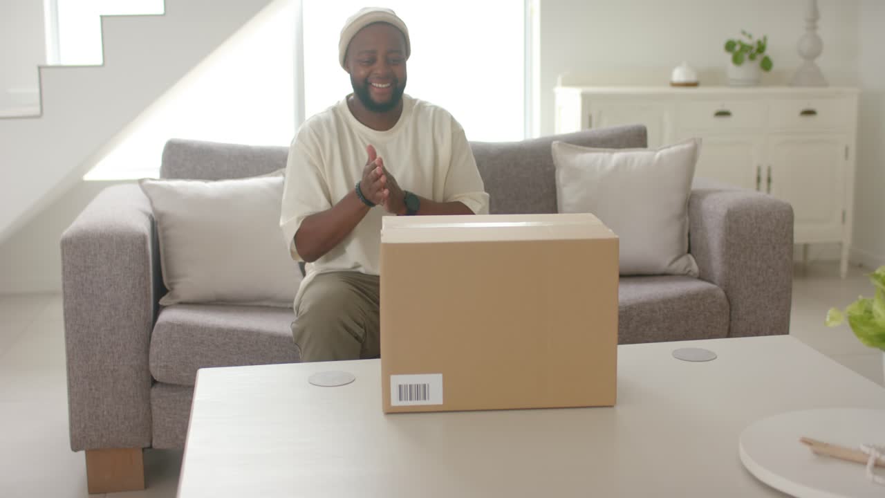 Adult man receiving box with barcode, placing on coffee table, preparing to open, wearing beanie
