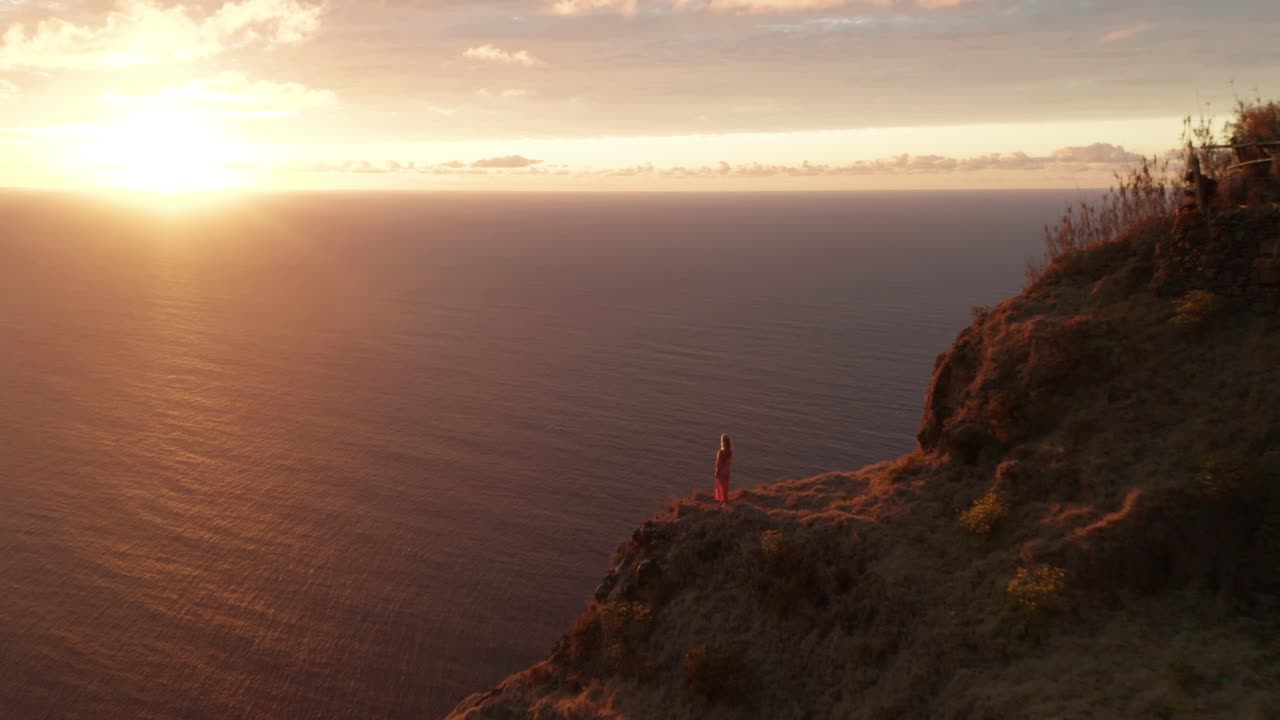 mujer mirando el océano atlántico desde un alto acantilado con una espectacular puesta de sol vívida