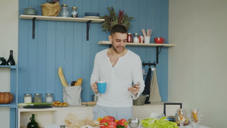 man using smartphone in kitchen while drinking coffee