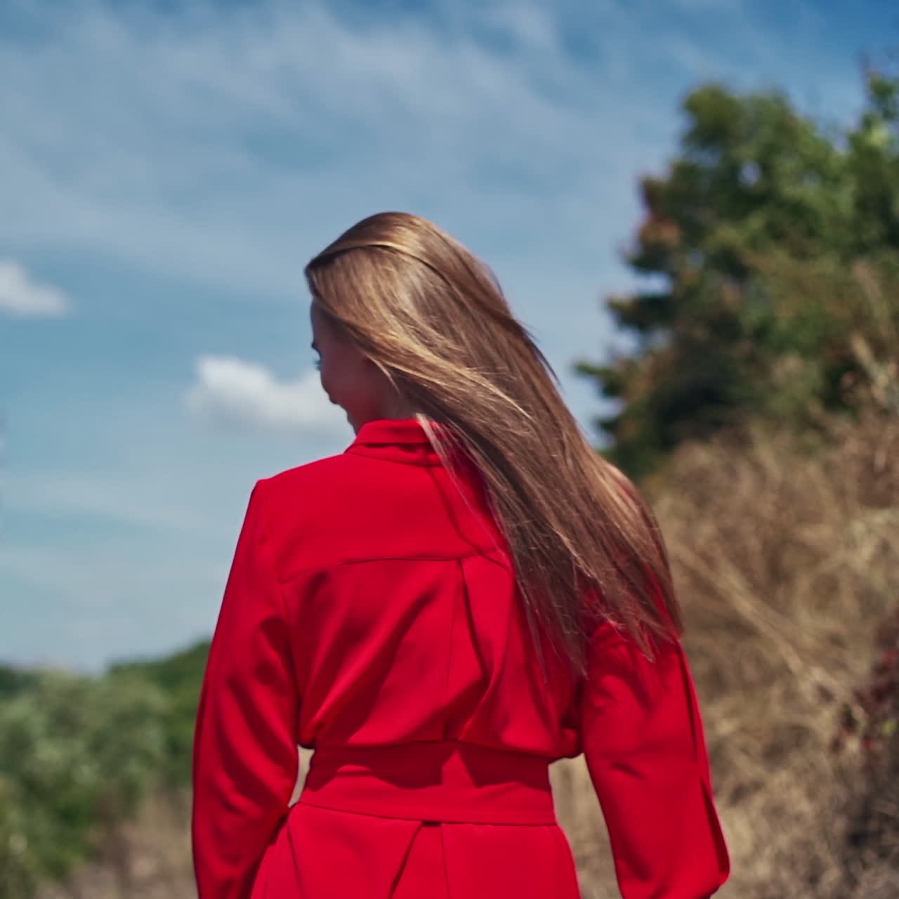 Sexy woman with long hair outdors. Backside view of a pretty woman in bright dress walking in nature. Slow motion.