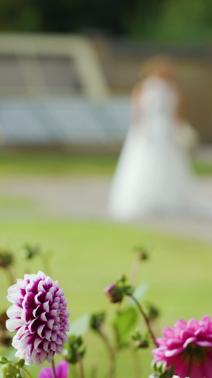 Brud i hvid kjole går bag farverige blomster, lav dybdeskarphed, blødt dagslys