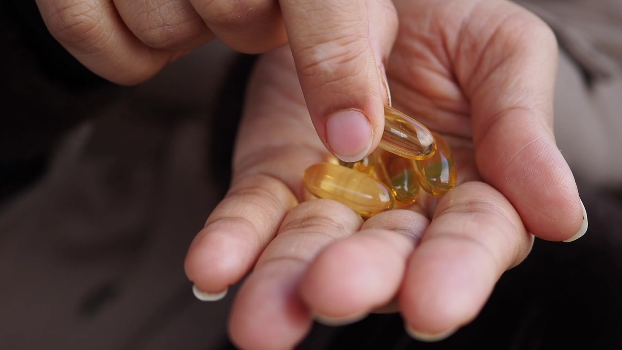 Close Up of Hand Holding and Examining Yellow Softgel Capsules