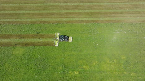 Aerial-establishing-view-of-a-tractor-mowing-a-fresh-green-grass-field,-a-farmer-in-a-modern-tractor-preparing-food-for-farm-animals,-sunny-summer-day,-wide-birdseye-drone-dolly-shot-moving-right