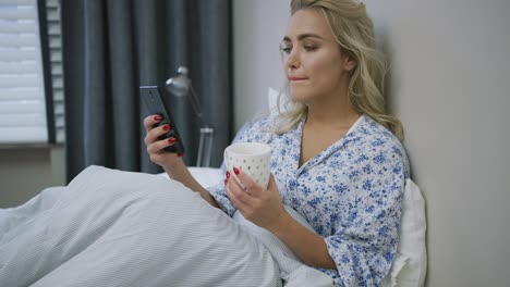 Woman-with-smartphone-and-mug-on-bed