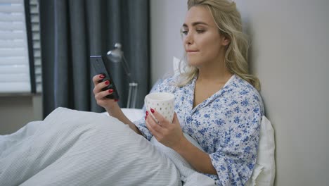 woman with smartphone and mug on bed