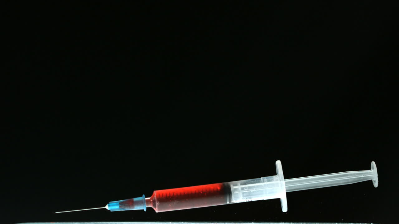 Siringa di sangue che cade e rimbalza su superficie nera