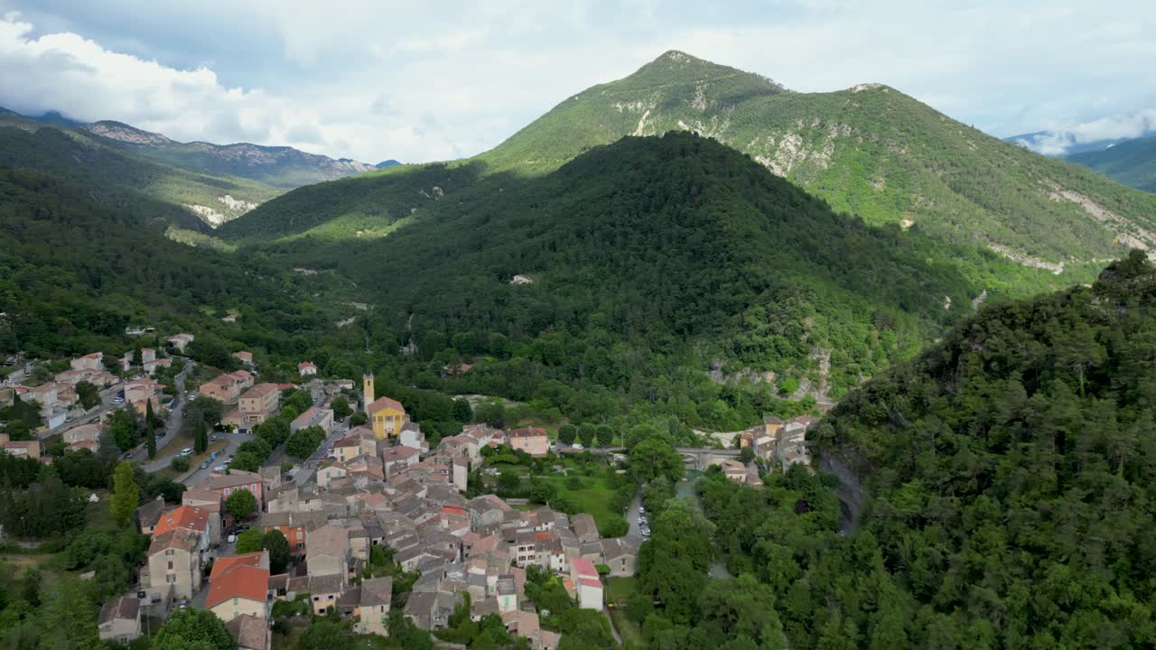 Aerial view of a quaint mountain village in the south of France, surrounded by lush greenery under the summer sun.