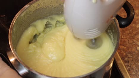 using a handheld whisk to mix a boiled milk frosting batter on a stove