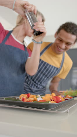vertical video of happy diverse couple seasoning vegetables in kitchen, slow motion