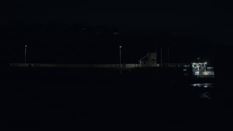 ferry boat waiting at long pier at night, distant static shot