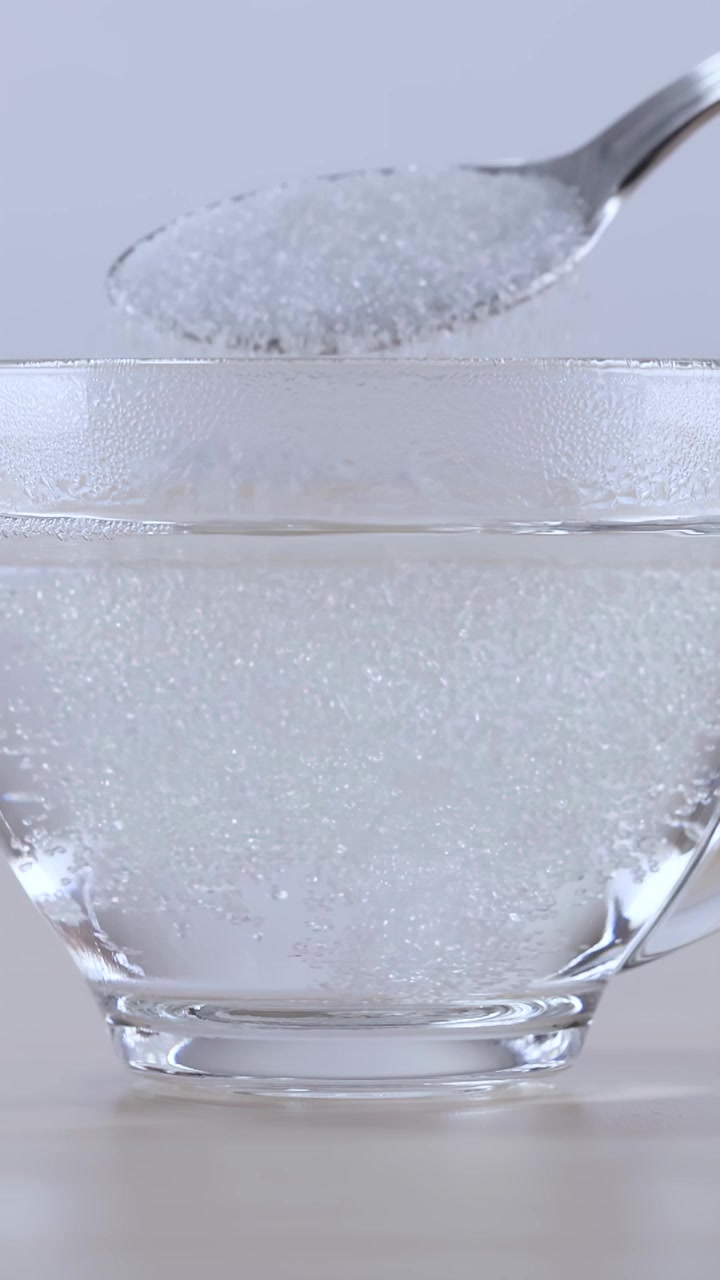 Zucchero che si versa in un bicchiere d'acqua