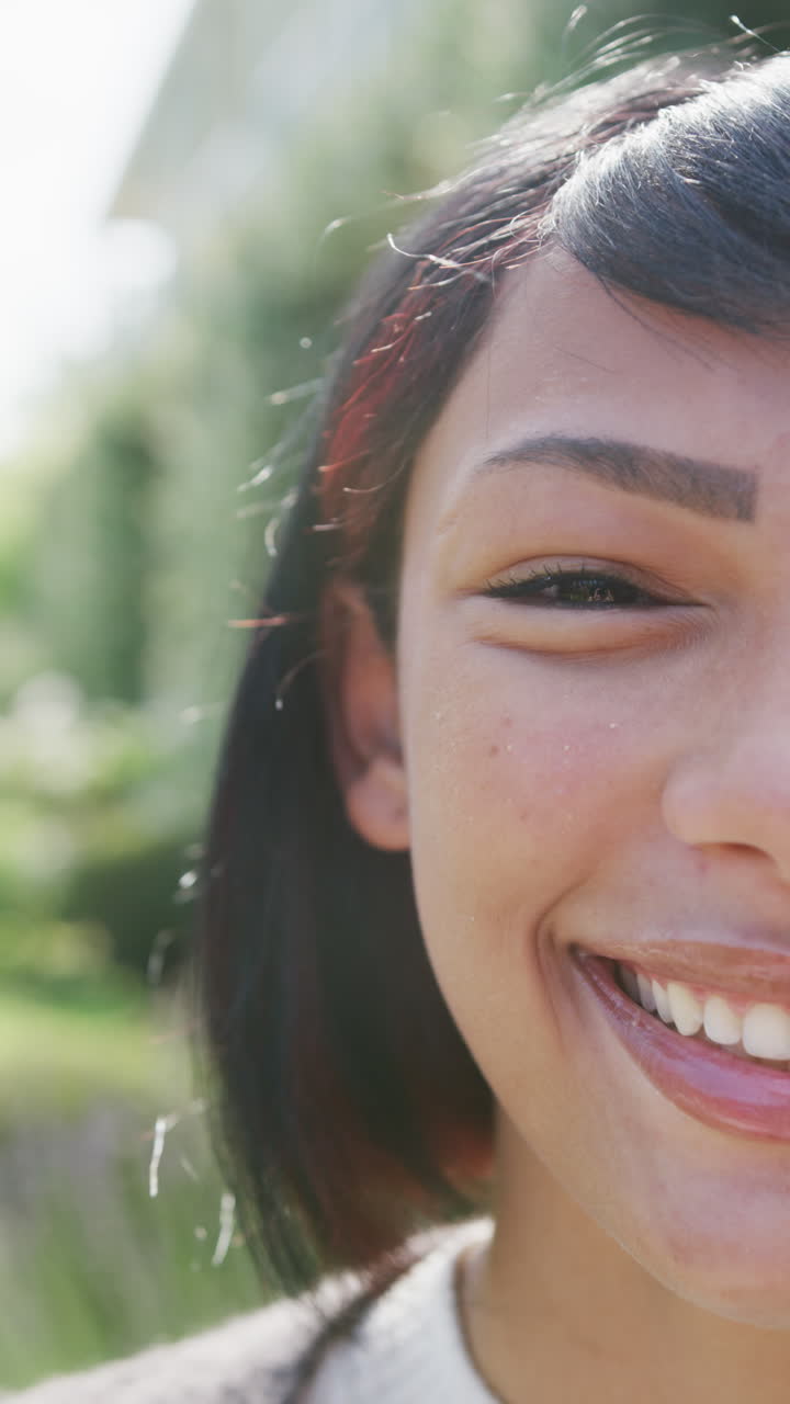 Vertical video of portrait of biracial teenager girl looking at camera and smiling, in slow motion