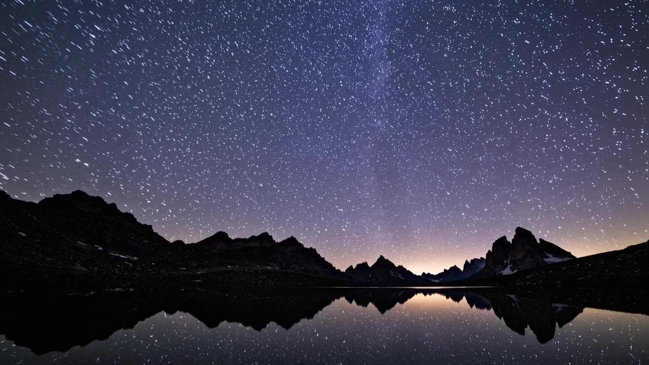 Time-lapse di scie stellari sopra un lago di montagna di notte